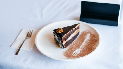 Tasty chocolate cake on a white plate standing at white cloth table