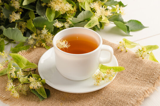 Herbal tea with lime blossom in a white cup on a white wooden table with flowers.