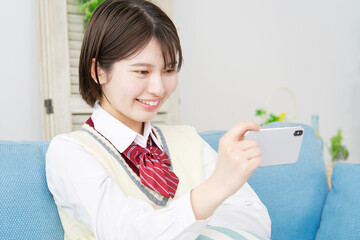 家でスマホで動画を見る女子高生