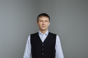 A man in a white shirt and a black vest on a gray background