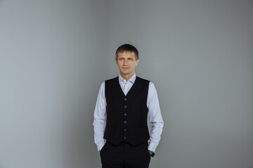 A man in a white shirt and a black vest on a gray background