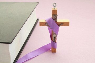 Christian religious wooden cross crucifix with violet ribbon and bible book on purple background. Catholic religion symbol. Good Friday, Lent Season, Palm Sunday, Ash Wednesday and Holy Week concept