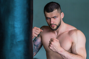 Strong young man boxer boxing in gym. Sporty male workout with punchbag boxing bag in sports club. Young man has fitness workout. Male athlete does exercise, sport.