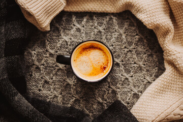 Top view of a black mug with strong aromatic coffee, which stands among warm wool sweaters. A hot drink in the cold season.