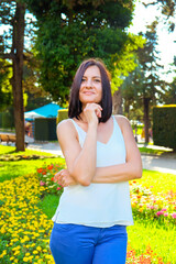 Romantic woman posing in colorful flowers. Cheerful, smiling, lucky woman in white blouse outdoors. Sunny summer day.