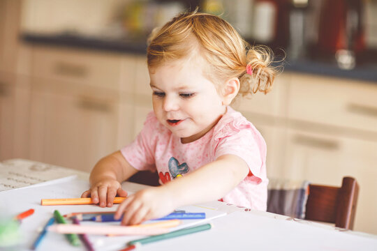 Cute adorable baby girl learning painting with pencils. Little toddler child drawing at home, using colorful felt tip pens. Healthy happy daughter experimenting with colors at home or nursery.