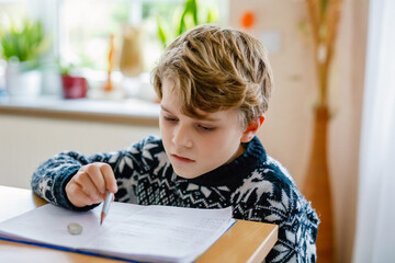 Hard-working happy school kid boy making homework during quarantine time from corona pandemic disease. Healthy child writing with pen, staying at home. Homeschooling concept