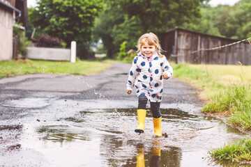 Little toddler girl wearing yellow rain boots, running and walking during sleet on rainy cloudy...