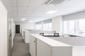 Fototapeta na wymiar Modern corporate open office in minimalist modern design in whites and greys, empty office workstations.