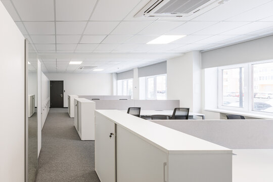Modern corporate open office in minimalist modern design in whites and greys, empty office workstations.