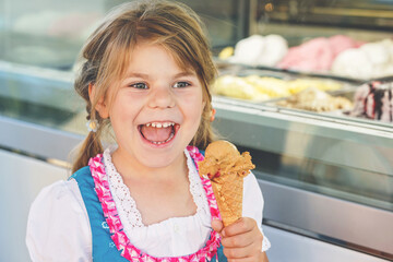Little preschool girl eating sweet ice cream in waffle cone on sunny summer day. Happy toddler...