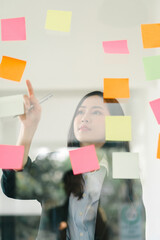 The concept of brainstorming is exemplified as a businesswoman shares ideas using Post-it notes, which she places on a glass wall.