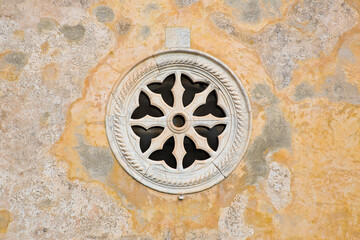 Medieval italian stone rose window against a plaster wall - Italy