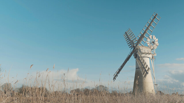 Windmill made of bricks and wood, large traditional wind mill in a meadow or field underneath a blue sky, Norfolk Broads landmarks