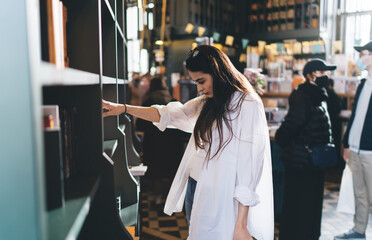 Naklejka premium Pensive woman choosing book in bookstore