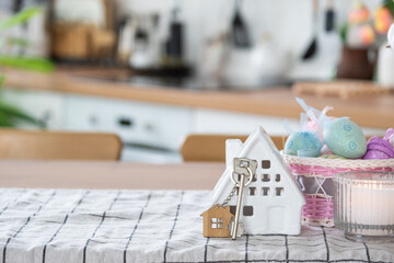 Key to house of cozy home with Easter decor with rabbit and eggs on table of kitchen. Building, design, project, moving to new house, mortgage, insurance, rent and purchase real estate