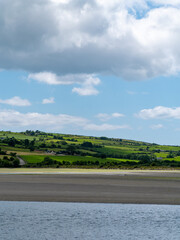 White clouds in the sky, countryside. Green hills on a summer day. Irish countryside, County Cork. Green grass field near body of water under white clouds and blue sky
