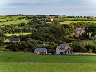 A European village among green fields, trees. Farmhouses in Ireland. Picturesque agricultural landscape. Green fields under a blue sky, houses on green grass field.