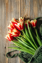Bouquet of fresh tulips in a string bag on a wooden background, top view, concept of mother's day, women's day, spring background with a bouquet of flowers, rustic style.