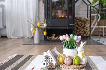Key to house near fireplace stove with fire and firewood. Cozy home hearth with easter decor, colorful eggs in a basket and bunny. Building, design, project, moving to new house, mortgage, rent and pu