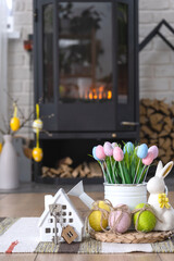 Key to house near fireplace stove with fire and firewood. Cozy home hearth with easter decor, colorful eggs in a basket and bunny. Building, design, project, moving to new house, mortgage, rent and pu