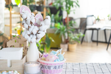 Easter decoration of colorful eggs in a basket and a rabbit on the kitchen table in a rustic style. Festive interior of a country house