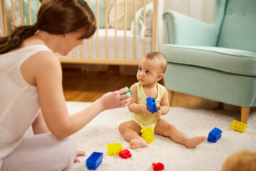 Obraz na płótnie Canvas Mother and her baby boy playing with colored toy blocks at home
