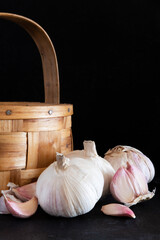 Garlic and garlic cloves next to a basket made of chestnut wood and isolated on a black background