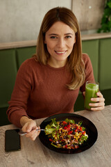 Mid adult woman enjoys eating salad and drinking smoothie in salad bar