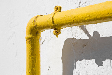 Methane gas and water yellow metal pipe against a white rough plaster wall