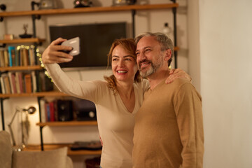 Cheerful mature couple taking selfie with smart phone at home