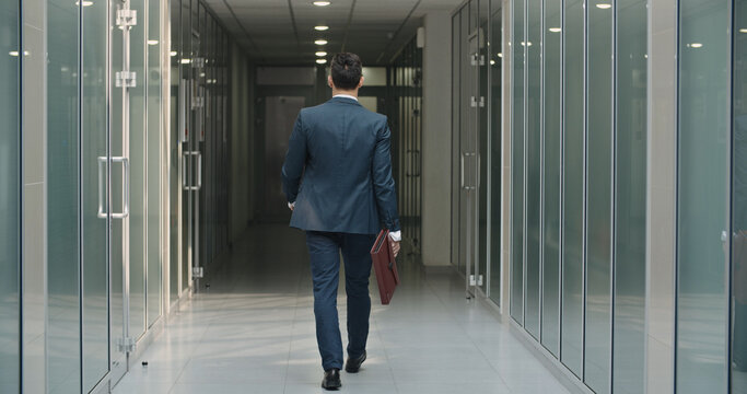 Rear View Of Classy Asian Businessman. The Man Holding Business Handbag With Office Formal Suit Walking In Office Building. A Student Walks Down The Hall During A Break At A Business University