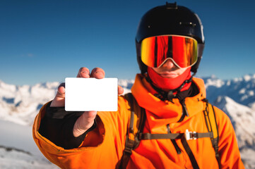 snowboarder holds an empty lift pass with a mountain in the background. A young man is holding an empty ski pass and looking at the camera. Concept illustrating ski entry fee - obrazy, fototapety, plakaty