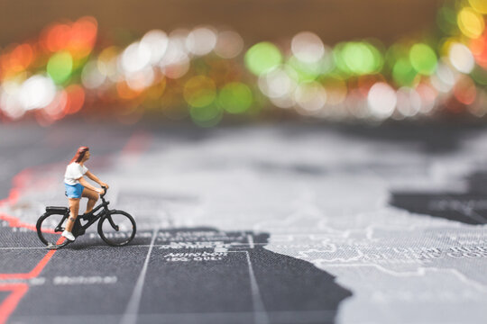 Miniature people travelers riding bicycle on world map