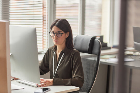 Portrait of businesswoman wearing glasses while using computer at workplace in office, copy space