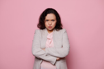 Fototapeta premium Angry dissatisfied middle-aged multiethnic woman in a light gray jacket, get bored upset, expressing worry anxiety, posing with lips pouted and arms folded on pink background. People Emotions Concepts