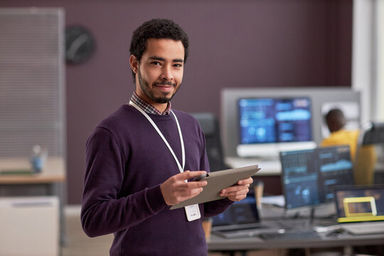 Waist up portrait of smiling software engineer holding digital tablet while standing in tech office, copy space