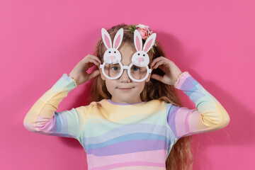 Cute little child girl wearing bunny ears glasses a on Easter day. Easter girl portrait on pink background, funny emotions, surprise.