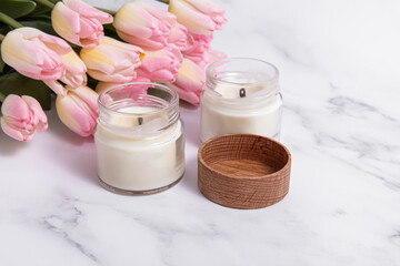 Two scented candles and pink tulips on marble background. Candles in glass