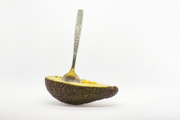 Half of an avocado with an old Soviet stainless spoon stuck into the pulp on a white background