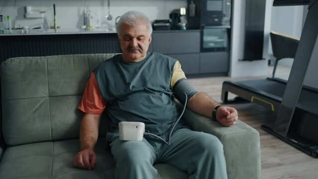 Senior Hypertensive Man Taking Blood Pressure And Pulse By Digital Blood Pressure Monitor