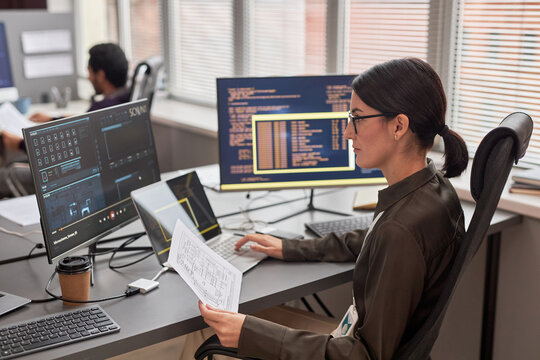 Side view portrait of female data engineer working with computers at desk in IT company office