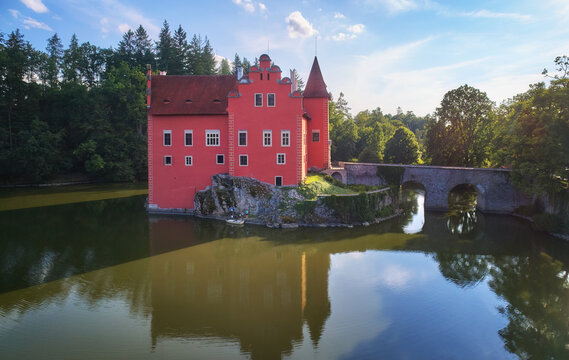 Aerial view of picturesque water castle Cervena Lhota, renaissance-style red château standing in the middle of a lake on a rock cliff,  stone bridge, south Bohemia, Czech Republic.