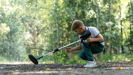 a boy with a metal detector is looking for treasure in the forest - obrazy, fototapety, plakaty