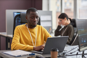 Portrait of young black man using laptop while working as software developer in IT company, copy...
