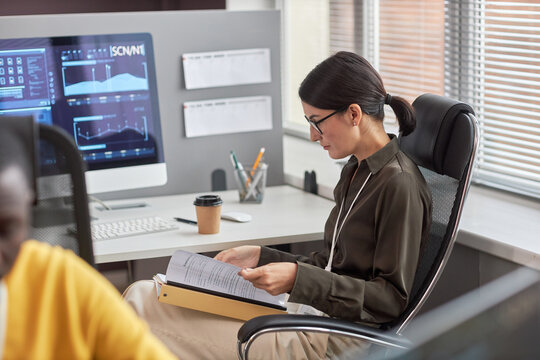 Side view portrait of female data scientist working with documentation at desk in office