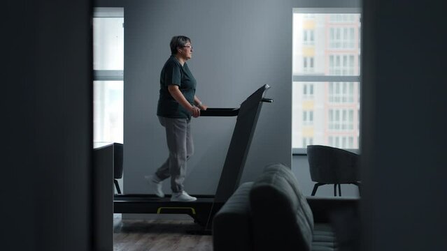 Senior Woman With Eyeglasses Training On Treadmill At Home, Fitness Workout For Saving Health