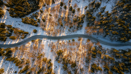 Drone top down on the road and a forest. A bird's eye view of the snowy landscape with the sun...