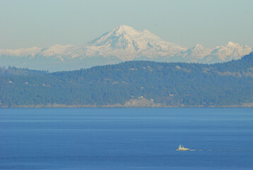A tugboat motors in front of snow covered Mount Baker on a calm and sunny winters day