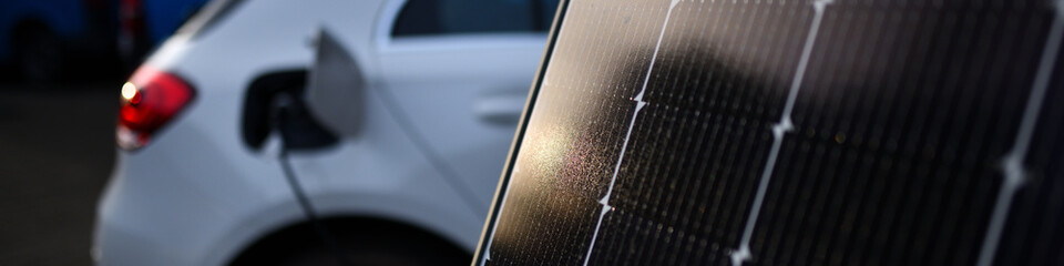 Elektroauto vor PV Solarpanel laden. Banner f&uuml;r Web Template mit Ladestecker im textfreiem Hintergrund als Antwort auf die Klimakrise. Frisch installiert vom Elektriker / Energieberater.